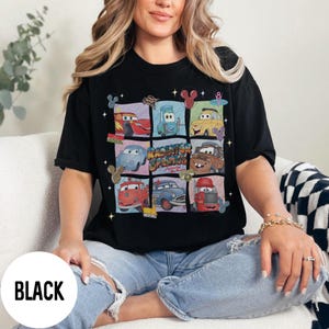 May include: Black t-shirt featuring a grid of cartoon cars from the movie Cars, with the text "Radiator Springs" in the center. The design includes various car characters in colorful squares. The word "BLACK" is printed on a white circle.