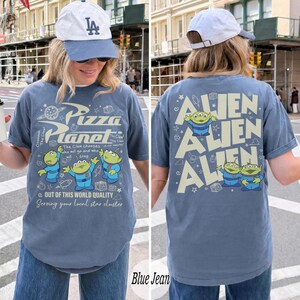 K&ouml;nnte beinhalten: Blaues Jeans-T-Shirt mit einem Pizza Planet-Motiv auf der Vorderseite und dem Text "Alien" auf der R&uuml;ckseite. Die Vorderseite zeigt das Pizza Planet-Logo und gr&uuml;ne Alien-Charaktere. Die R&uuml;ckseite wiederholt das Wort "Alien" mit Alien-Charakteren.