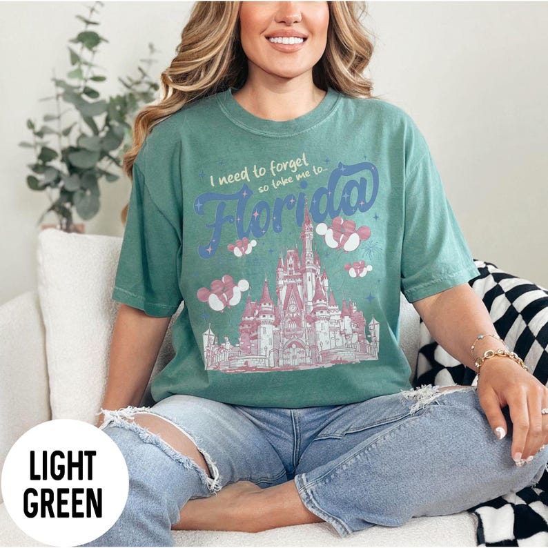 May include: Light green t-shirt with the text "I need to forget so take me to Florida" above a pink and white illustration of a castle. The shirt is a light green color.