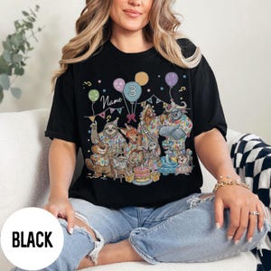 以下が含まれることがあります： 黒いTシャツ。カラフルな誕生日パーティーのデザインで、漫画の動物、風船、ケーキが描かれています。シャツには「Name」という文字と数字の「3」がプリントされています。画像の下部には「BLACK」という文字がプリントされています。