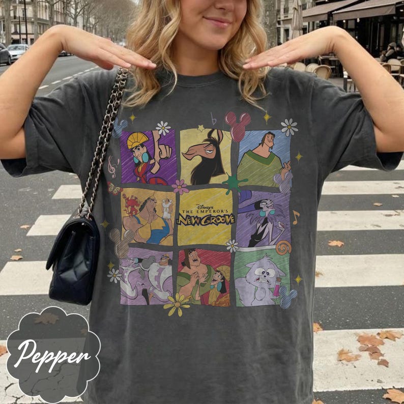 May include: A charcoal gray short-sleeve t-shirt featuring a grid of colorful illustrations of characters from the movie The Emperor's New Groove, including Kuzco, Pacha, Yzma, and Kronk, with the movie title text centered in the middle.