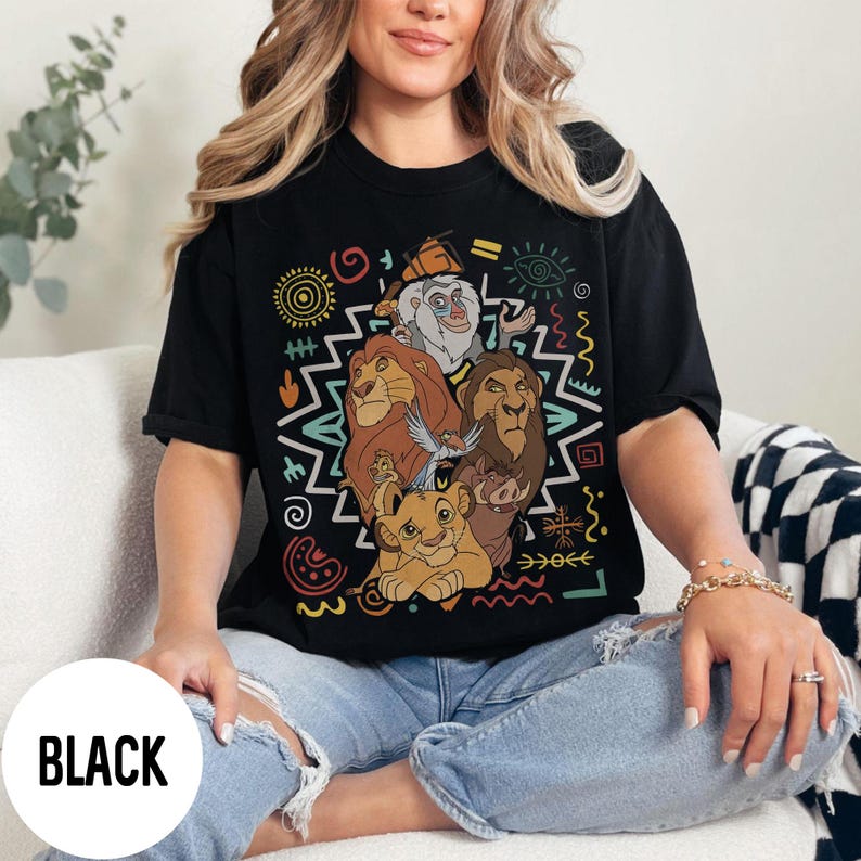 Puede incluir: Camiseta negra con un gr&aacute;fico colorido de personajes de El Rey Le&oacute;n. El dise&ntilde;o incluye leones y otros personajes, rodeados de patrones tribales. La palabra "BLACK" est&aacute; impresa en la parte inferior de la camiseta.