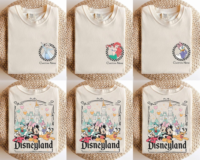Pu&ograve; includere: T-shirt color crema con disegni di personaggi Disney. Alcune magliette presentano Elsa, Ariel e Paperina in cornici circolari a scacchi con il testo "Custom Name". Altre magliette mostrano una grafica di Disneyland con vari personaggi e la scritta "Disneyland 1955".