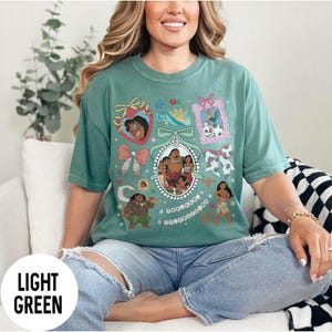 Pu&ograve; includere: T-shirt verde chiaro con un ritratto ovale centrale di una famiglia, circondato da illustrazioni di personaggi incorniciate e fiocchi. La maglietta ha il testo "LIGHT GREEN" in basso a sinistra. Il design include personaggi dei cartoni animati ed elementi decorativi.