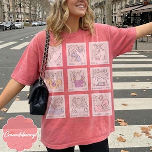 May include: A faded red t-shirt featuring nine cartoon illustrations of animated characters with dates. The text "Crunchberry" is at the bottom left. The shirt is worn by a person on a crosswalk.