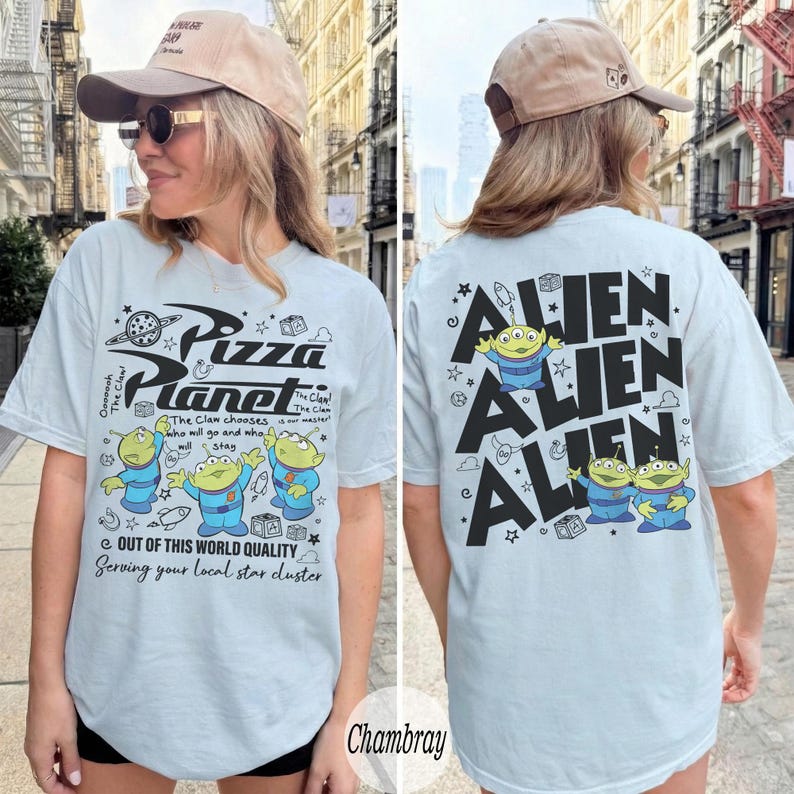 K&ouml;nnte beinhalten: Hellblaues T-Shirt mit Pizza Planet-Design und Alien-Charakteren. Auf der Vorderseite befindet sich das Pizza Planet-Logo und Text. Auf der R&uuml;ckseite steht das Wort "Alien" mehrfach. Ein l&auml;ssiges Kleidungsst&uuml;ck.