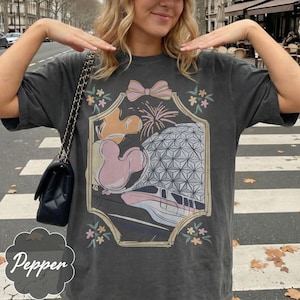 May include: Dark gray t-shirt with a colorful graphic featuring a pink bow, fireworks, a Mickey Mouse balloon, and a geometric sphere. The word "Pepper" is written in a decorative font at the bottom.