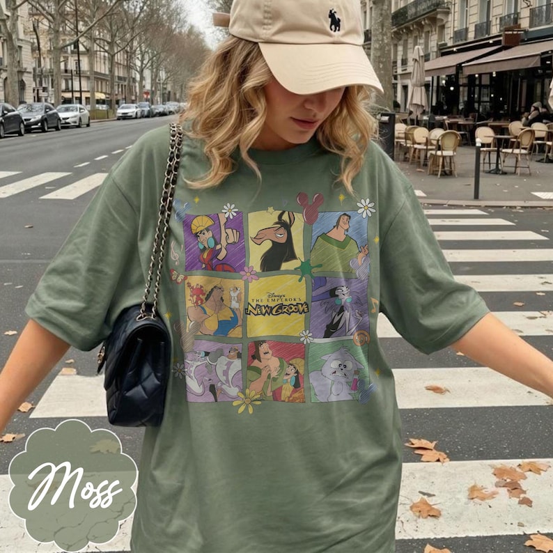 May include: An olive green t-shirt featuring a grid of colorful graphic illustrations from the movie The Emperor's New Groove, including characters like Kuzco, Pacha, and Yzma, with the movie title text centered in the middle of the design.