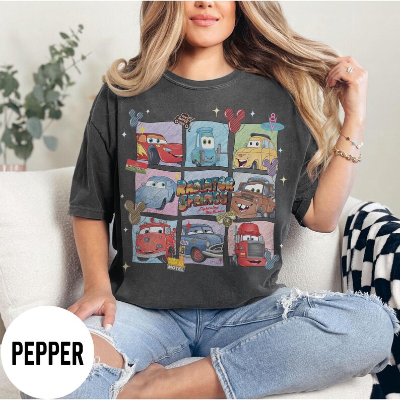 May include: Dark grey t-shirt featuring a grid of cartoon cars from the movie Cars, with the text "Radiator Springs" and other graphics. The shirt is a comfortable, casual style.