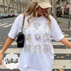 May include: White t-shirt featuring a grid of cartoon sketches of animated characters. The shirt has a crew neck and short sleeves. The word "White" is written in a decorative font at the bottom of the shirt.