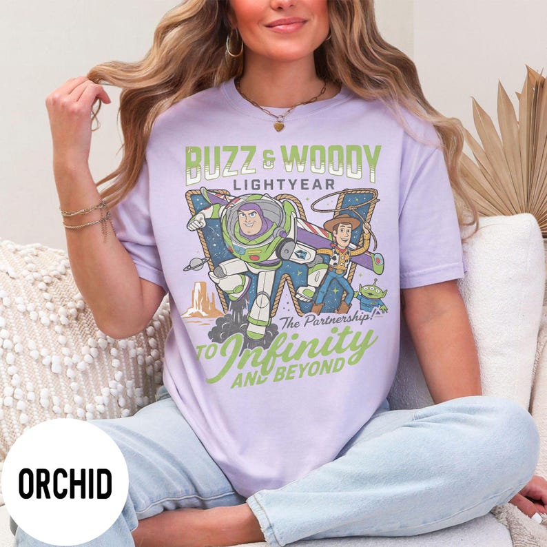 May include: Lilac t-shirt featuring Buzz Lightyear and Woody from Toy Story. The graphic includes the text "Buzz & Woody Lightyear" and "To Infinity and Beyond". The shirt has a relaxed fit.