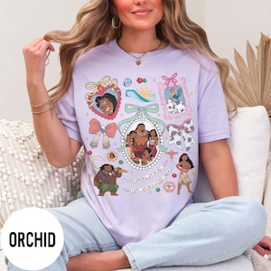 Pu&ograve; includere: T-shirt color orchidea con un design grafico colorato con personaggi ed elementi di un popolare film d'animazione. Il design include ritratti incorniciati, fiocchi e la scritta "THE SEA UT CALLS ME".