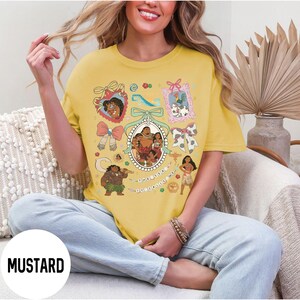 Pu&ograve; includere: T-shirt color senape con un design grafico colorato con personaggi di cartoni animati. Il design include ritratti incorniciati, fiocchi e la scritta "The Ocean Calls Me". La maglietta ha una vestibilit&agrave; ampia.