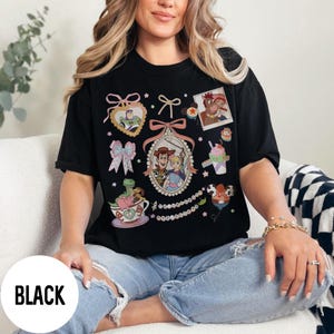 May include: Black t-shirt featuring various cartoon character graphics. The shirt includes images of characters in heart-shaped frames, bows, and a framed photo. The word "BLACK" is printed on the bottom of the shirt.