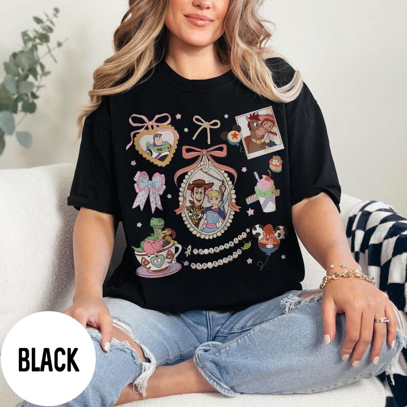 May include: Black t-shirt featuring various cartoon character graphics. The shirt includes images of characters in heart-shaped frames, bows, and a framed photo. The word "BLACK" is printed on the bottom of the shirt.