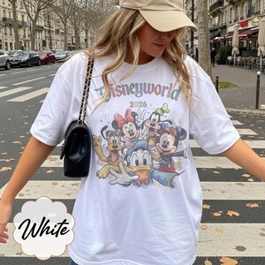 Pu&ograve; includere: T-shirt bianco con una grafica colorata dei personaggi Disney, tra cui Topolino e Minnie, e Paperino. La maglietta ha la scritta "Disneyworld 2026" stampata sul davanti. La maglietta &egrave; in stile casual e oversize.