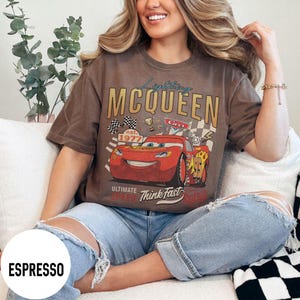 Op de afbeelding: Espresso-kleurig T-shirt met een afbeelding van Lightning McQueen uit de film Cars. Het ontwerp bevat de tekst "Lightning McQueen", "Cars", "est. 1977" en "Ultimate Speed Think Fast". Het shirt heeft een vintage, distressed look.