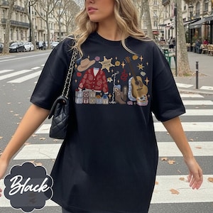 May include: A black t-shirt featuring a graphic print with a tan cowboy hat, a red paisley cardigan, a sheriff star badge labeled Sheriff Taylor, a brown acoustic guitar, a cowboy boot, and blocks spelling out the words Toy Story.