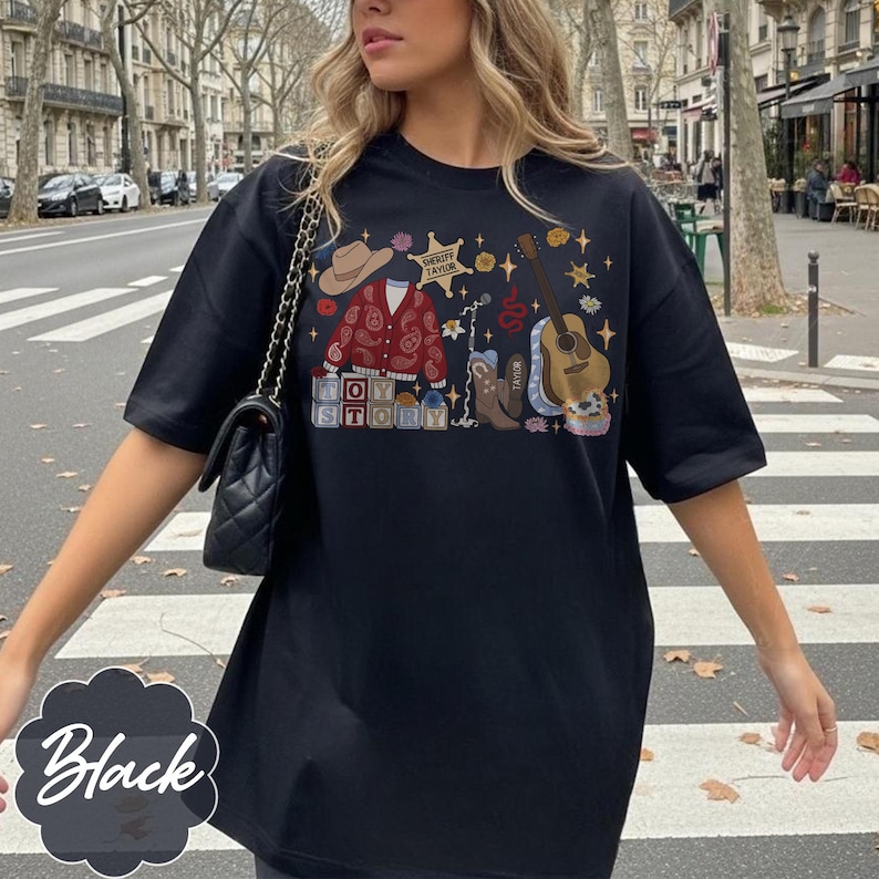 May include: A black t-shirt featuring a graphic print with a tan cowboy hat, a red paisley cardigan, a sheriff star badge labeled Sheriff Taylor, a brown acoustic guitar, a cowboy boot, and blocks spelling out the words Toy Story.