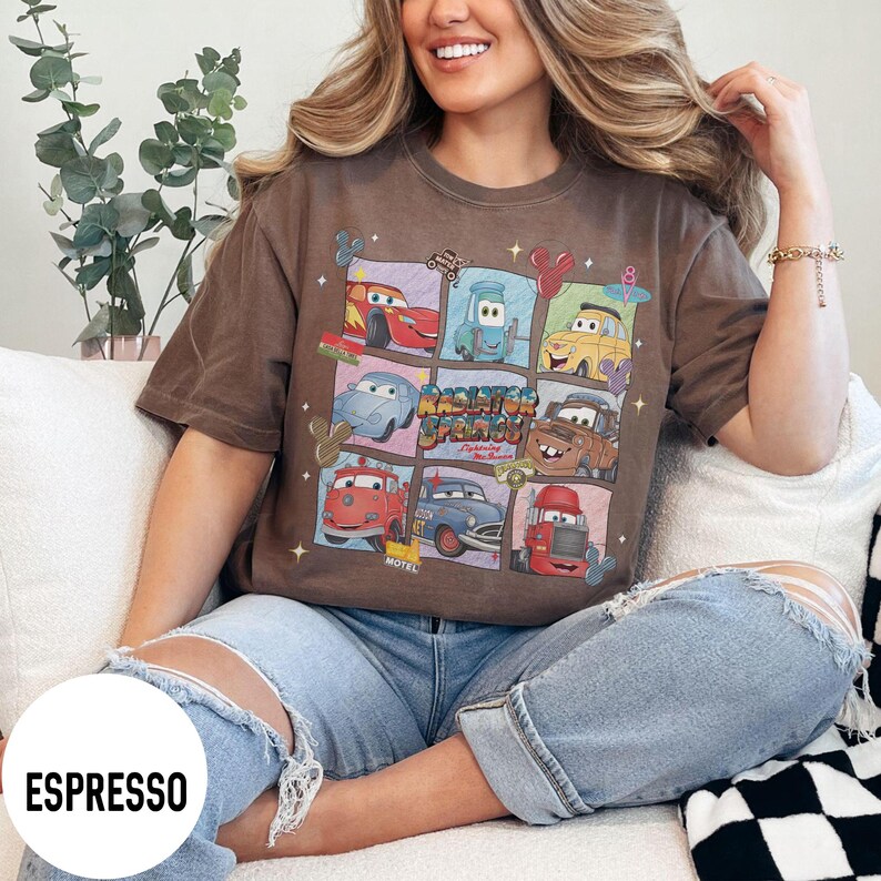 May include: Espresso-colored t-shirt featuring a colorful graphic of characters from the movie Cars. The design includes various car illustrations and the text "Radiator Springs". The shirt is a comfortable, casual style.