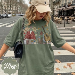 May include: An olive green t-shirt featuring a graphic print of a cowboy hat, a red paisley cardigan, a sheriff star badge labeled Sheriff Taylor, a microphone, a brown acoustic guitar, a cowboy boot, and blocks spelling out Toy Story.