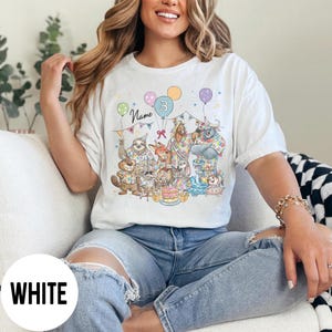 以下が含まれることがあります： 誕生日を祝う擬人化された動物たちのカラフルなイラストが描かれた白いTシャツ。デザインには風船、ケーキ、数字の3が含まれています。「Name」という文字も表示されています。