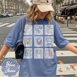 May include: Blue jean short-sleeve t-shirt featuring a grid of cartoon sketches of Disney princesses with their names and years. The shirt is a light blue color and has the words "Blue Jean" printed on the bottom left.