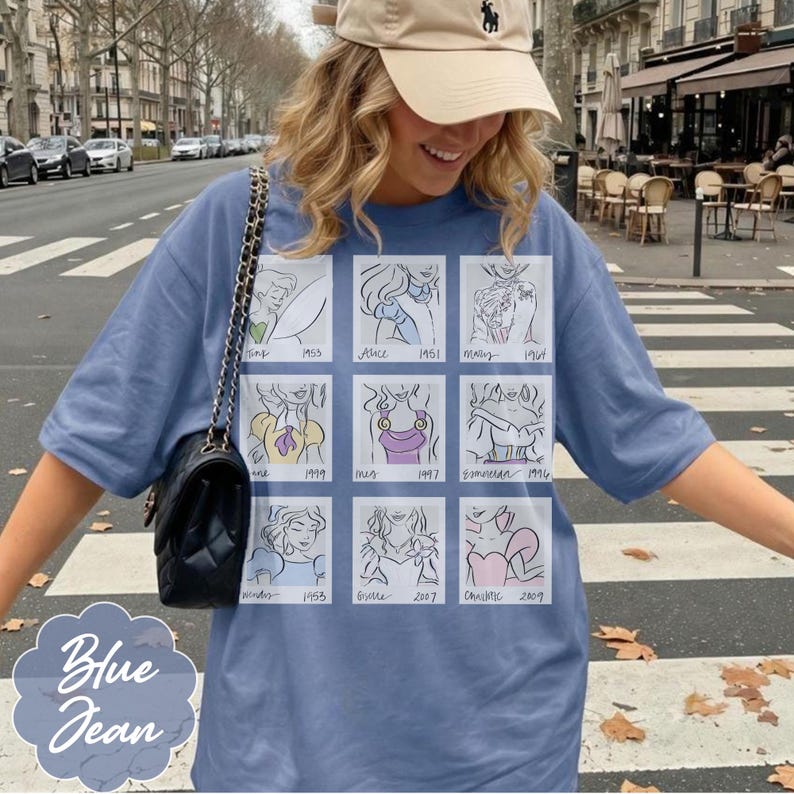 May include: Blue jean short-sleeve t-shirt featuring a grid of cartoon sketches of Disney princesses with their names and years. The shirt is a light blue color and has the words "Blue Jean" printed on the bottom left.