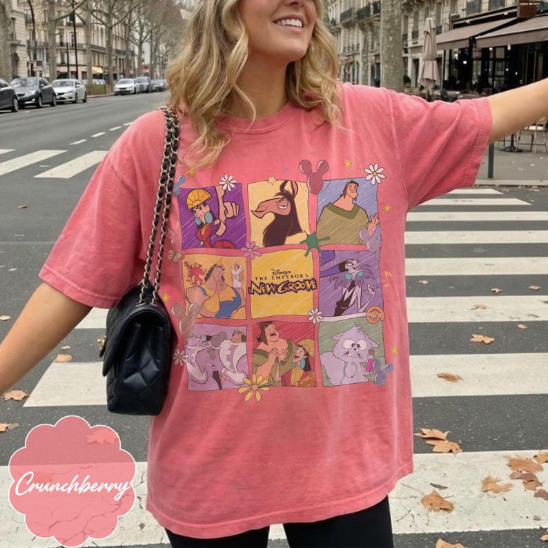 May include: A coral-colored short-sleeve t-shirt featuring a grid of colorful cartoon characters from Disney's The Emperor's New Groove. The graphic includes Kuzco, Pacha, Yzma, and Kronk, with the movie title text centered in the middle square.