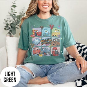 May include: Light green t-shirt featuring a grid of cartoon cars with the text "Radiator Springs". The shirt has a vintage, faded look. The cars are in various colors, including red, blue, and yellow. The shirt is a comfortable, casual style.