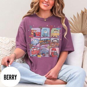 May include: Berry-colored t-shirt featuring a grid of cartoon cars from the movie Cars, with the text "Radiator Springs". The design includes various car characters in different squares. The shirt is a short-sleeved, crew neck style.