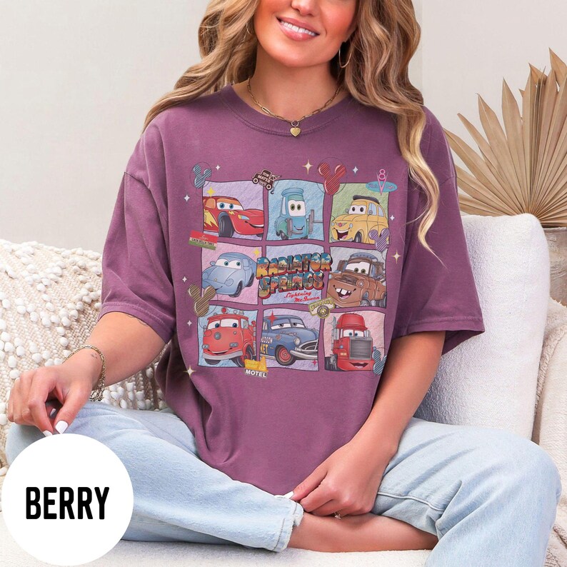 May include: Berry-colored t-shirt featuring a grid of cartoon cars from the movie Cars, with the text "Radiator Springs". The design includes various car characters in different squares. The shirt is a short-sleeved, crew neck style.