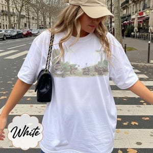 Puede incluir: Camiseta blanca con una ilustraci&oacute;n de dibujos animados de Grogu de The Mandalorian. El dise&ntilde;o muestra a Grogu en varias poses con un fondo de bosque. La palabra "White" est&aacute; escrita en una fuente decorativa en la parte inferior de la camiseta.