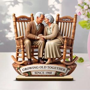 May include: A decorative figurine of an elderly couple sitting in rocking chairs, holding hands. The chairs are wooden, and the base has a banner that reads "GROWING OLD TOGETHER SINCE 1960". The chairs are labeled "Charlie" and "Sophia".