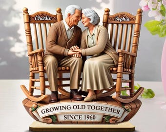 May include: A decorative figurine of an elderly couple sitting in rocking chairs, holding hands. The chairs are wooden, and the base has a banner that reads "GROWING OLD TOGETHER SINCE 1960". The chairs are labeled "Charlie" and "Sophia".