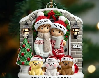 May include: A Christmas ornament featuring a couple and three dogs, all wearing Santa hats. The ornament has the names "Thomas" and "Natalie" on the hats of the couple, and "Jelly", "Mimi", and "Bella" on the dogs' hats. The text "YOU, ME & THE DOGS" is at the bottom.
