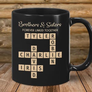 May include: Black ceramic mug with the words "Brothers & Sisters" and "FOREVER LINKED TOGETHER" in gold script. The mug features a crossword-style design with names spelled out using Scrabble tiles. The names include Tyler, Charlie, Iris, David, and others.