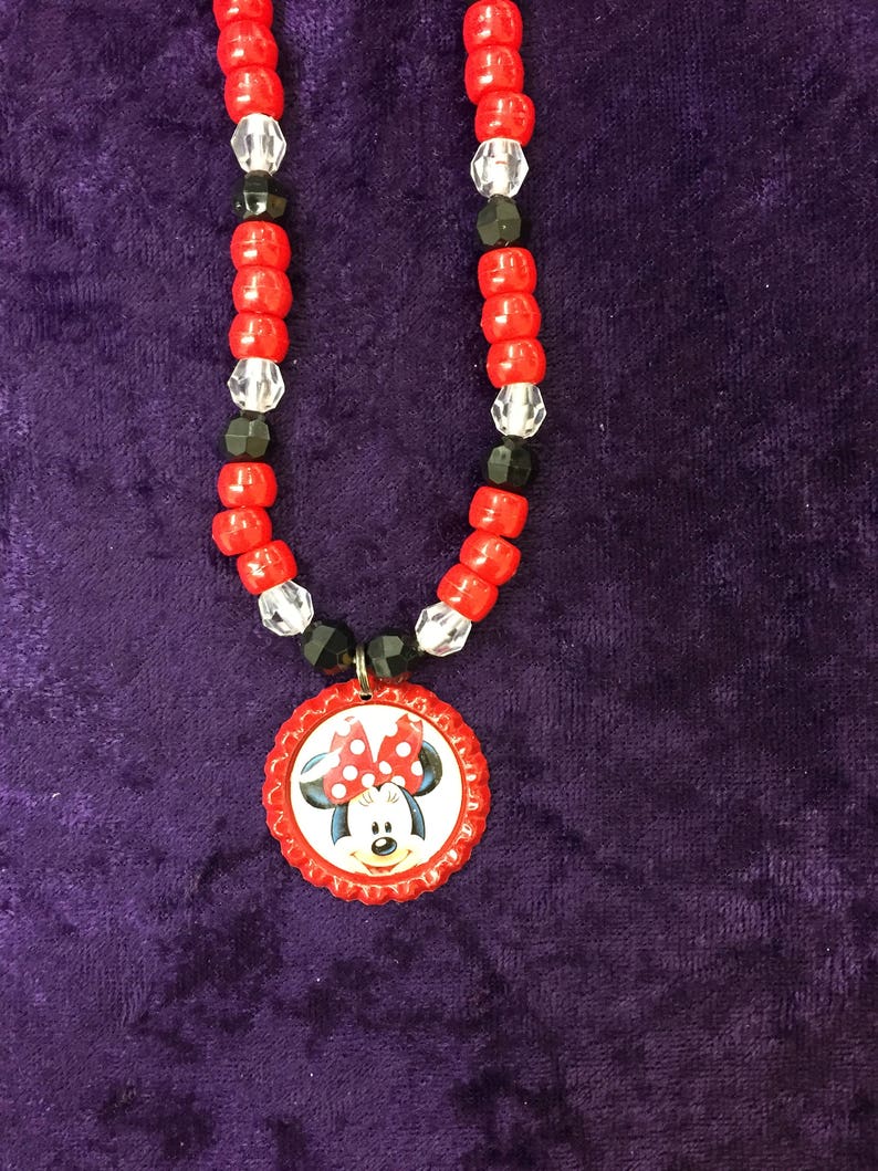 May include: A red beaded necklace with a Minnie Mouse pendant. The necklace features red, black, and clear beads. The pendant is a red bottle cap with a Minnie Mouse graphic.