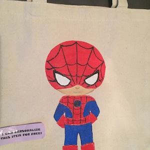 Puede incluir: Una bolsa de lona blanca con un dise&ntilde;o pintado a mano de un Spiderman de dibujos animados. Spiderman lleva un traje rojo y azul con un dise&ntilde;o de telara&ntilde;a negra. La bolsa tiene una etiqueta que dice "&iexcl;Puedo personalizar este art&iacute;culo gratis!"