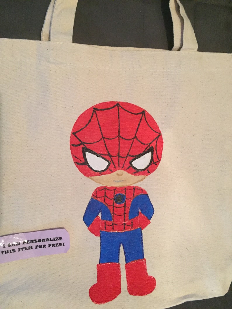 Puede incluir: Una bolsa de lona blanca con un dise&ntilde;o pintado a mano de un Spiderman de dibujos animados. Spiderman lleva un traje rojo y azul con un dise&ntilde;o de telara&ntilde;a negra. La bolsa tiene una etiqueta que dice "&iexcl;Puedo personalizar este art&iacute;culo gratis!"