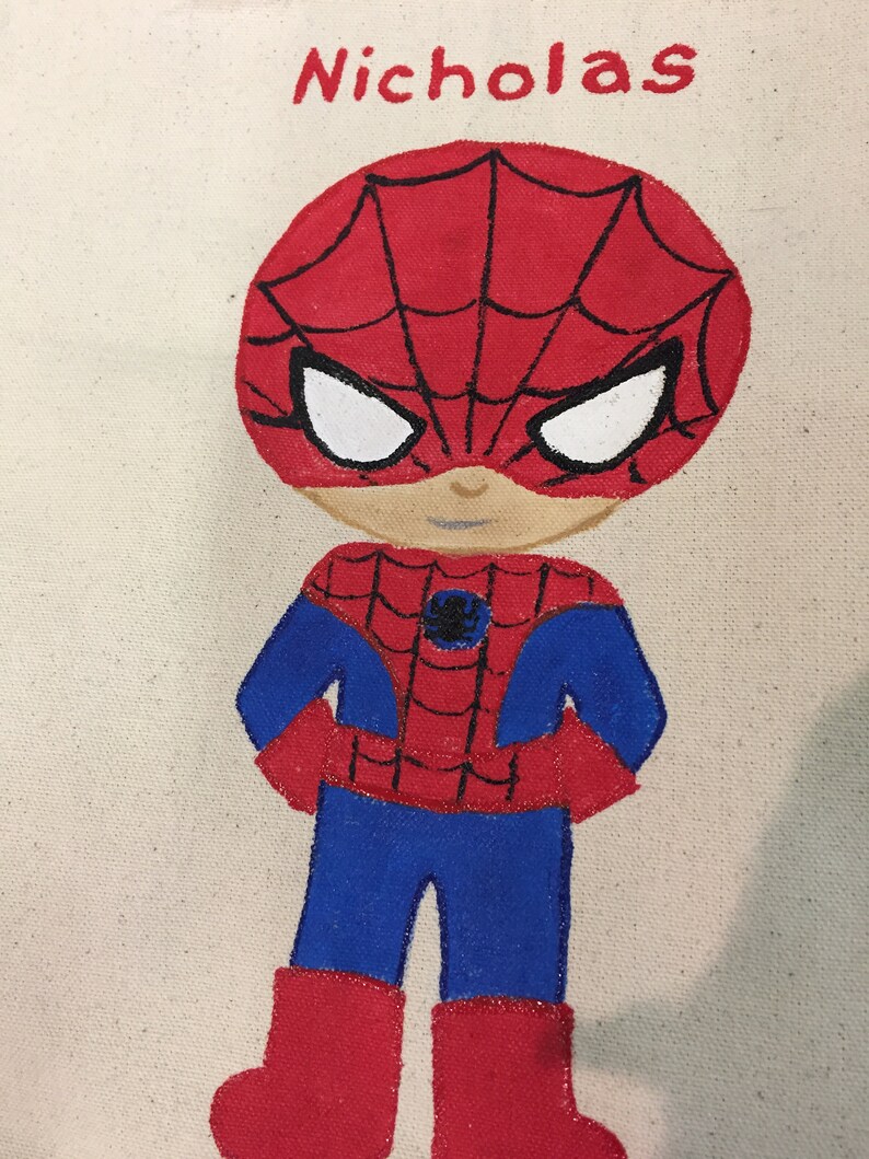 Puede incluir: Una bolsa de lona pintada a mano con una ilustraci&oacute;n de dibujos animados de Spiderman en rojo y azul, con el nombre "Nicholas" escrito sobre el personaje.