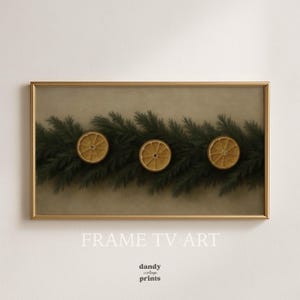 Pode incluir: Impressão emoldurada com uma grinalda de agulhas de pinheiro verdes e três rodelas de laranja secas. A obra de arte tem uma moldura dourada e um fundo neutro. O texto "FRAME TV ART" e "dandy vintage prints" está na parte inferior.