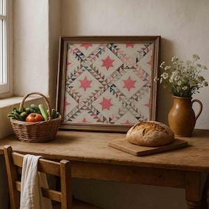 May include: A framed quilt with a star pattern in pink and cream tones sits on a wooden table. A basket of vegetables, a loaf of bread, and a vase of flowers complete the rustic scene. The table is made of wood.