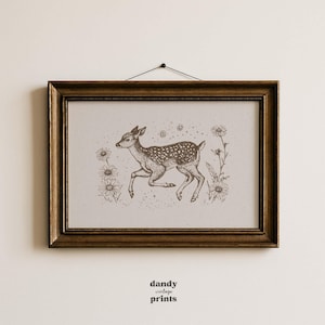 May include: A framed print featuring a sepia-toned illustration of a spotted fawn leaping through a field of daisies. The artwork is set within a dark brown, ornate wooden frame, and the text "dandy vintage prints" is visible at the bottom.