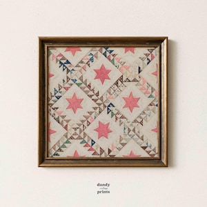 Printable vintage textile wall art featuring an antique quilt design of stars within squares in pinks, blues and beige. Displayed in a square antique brass frame on a white wall.