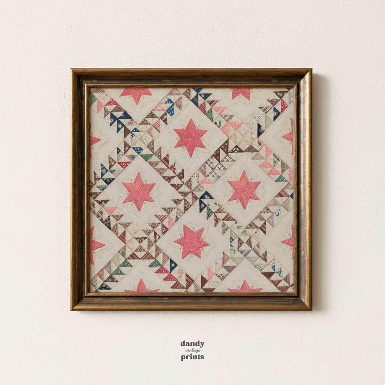 Printable vintage textile wall art featuring an antique quilt design of stars within squares in pinks, blues and beige. Displayed in a square antique brass frame on a white wall.