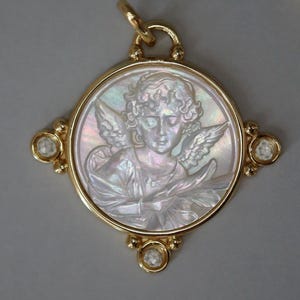 May include: Gold pendant featuring a carved mother-of-pearl cameo of an angel with wings. The pendant has a round frame with four diamond accents and a loop for a chain. The angel is depicted in a classical style.