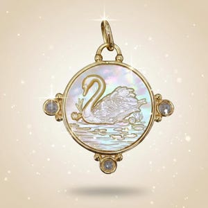 Può includere: Ciondolo in oro con design a cigno. Il ciondolo presenta un centro rotondo in madreperla con un'illustrazione dettagliata di un cigno. È impreziosito da piccole gemme trasparenti e da un'ansa decorativa.