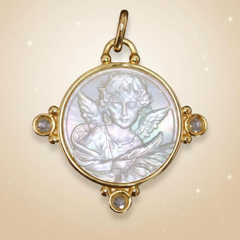 May include: A gold-toned pendant with a circular, mother-of-pearl cameo featuring an angel. The pendant has four decorative accents with clear gemstones. The angel has detailed wings and holds an object. The pendant is suspended from a gold bail.