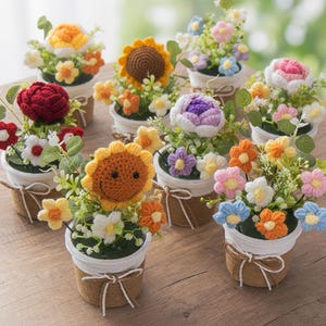 May include: A selection of handmade crochet flower arrangements in small pots. The flowers include sunflowers, roses, and other colourful blooms in shades of orange, yellow, pink, purple, and blue. The pots are wrapped with twine and white ribbon.